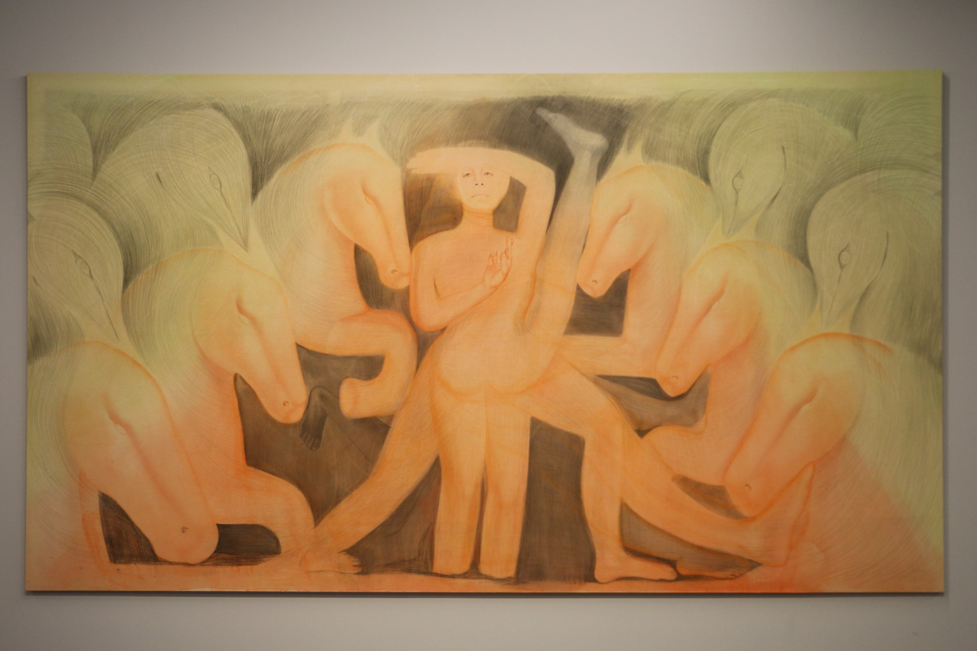 A large painting is hung on a wall. It has a central female figure which has multiple legs standing in various positions. Horses and bird figures stand either side of the figure with sketchy mark making and air brush techniques.