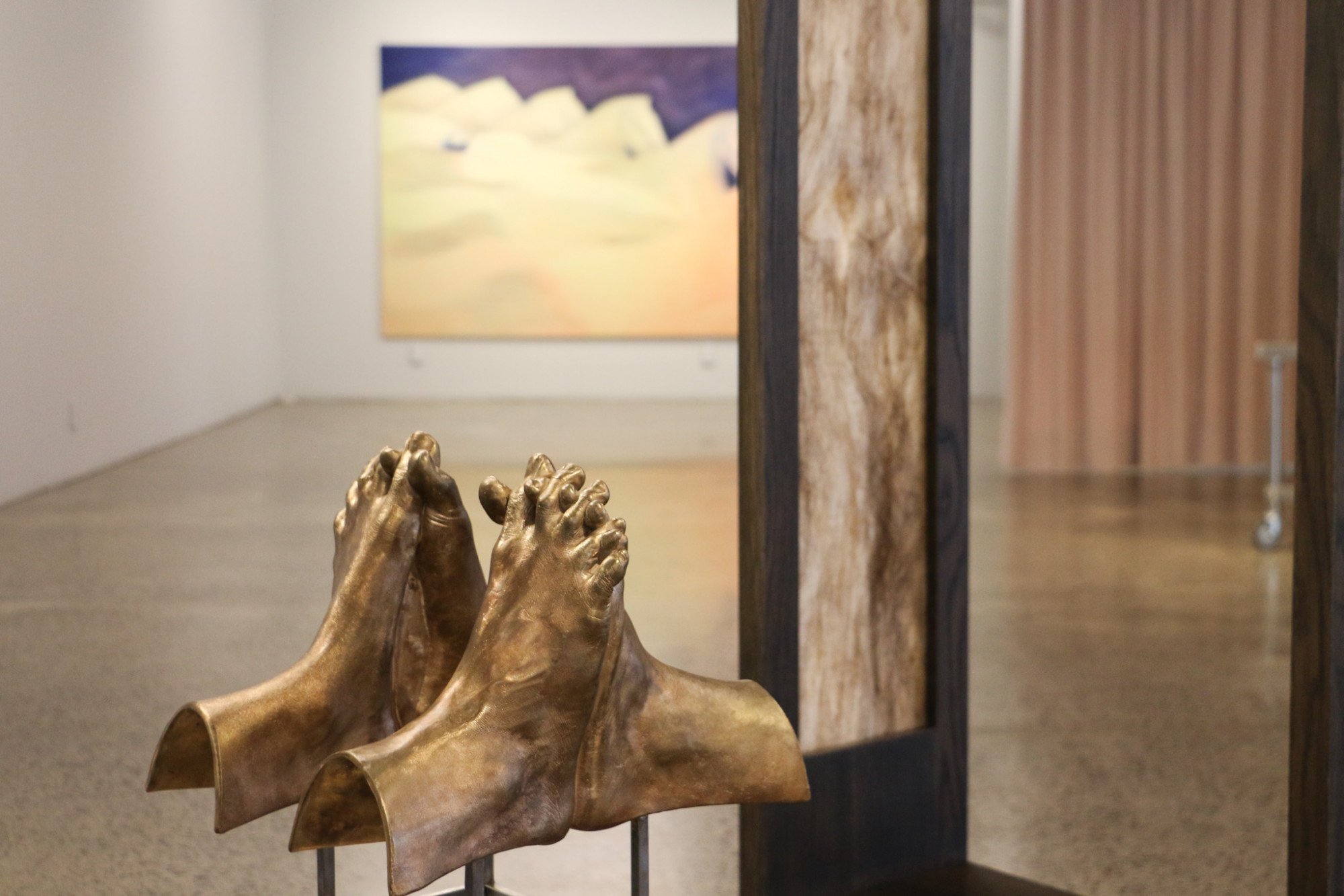 A structure holds up two sets of feet with intertwined toes cast in bronze.