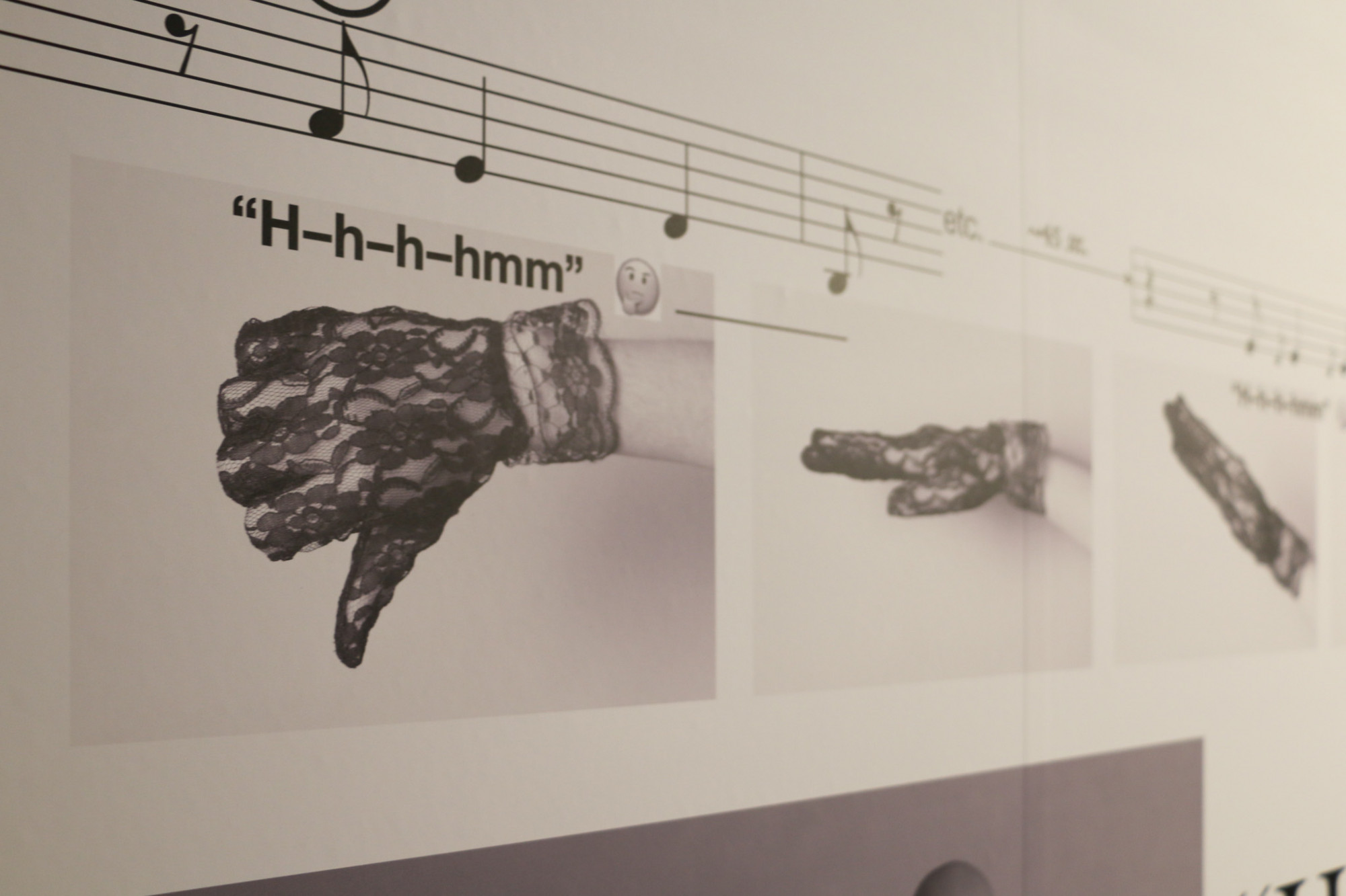 A close up of the wall featuring written music text and images of hands doing different gestures wearing black lace gloves.