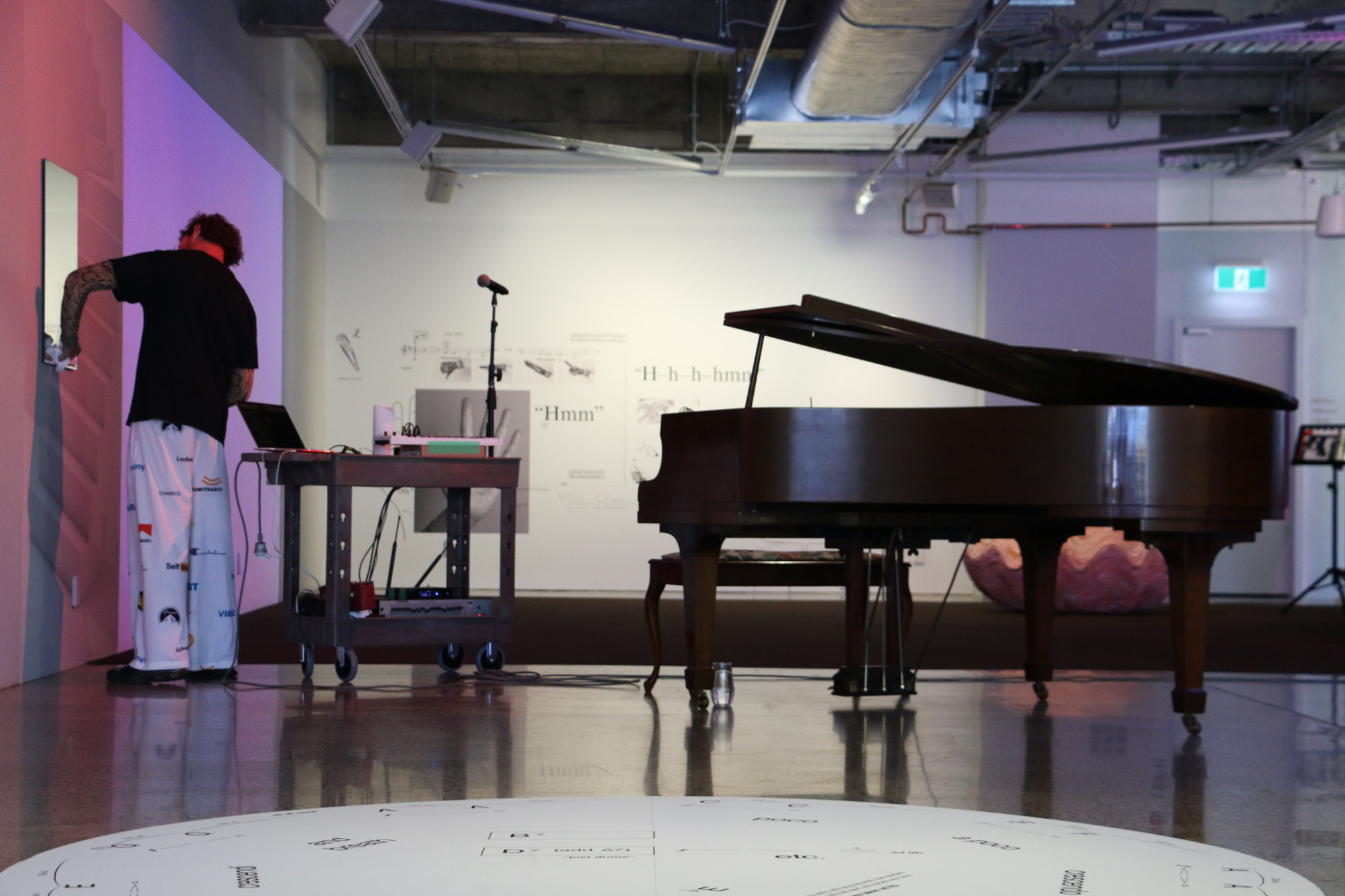 A person is writing on a mirror, there is a piano and other technical equipment next to them.
