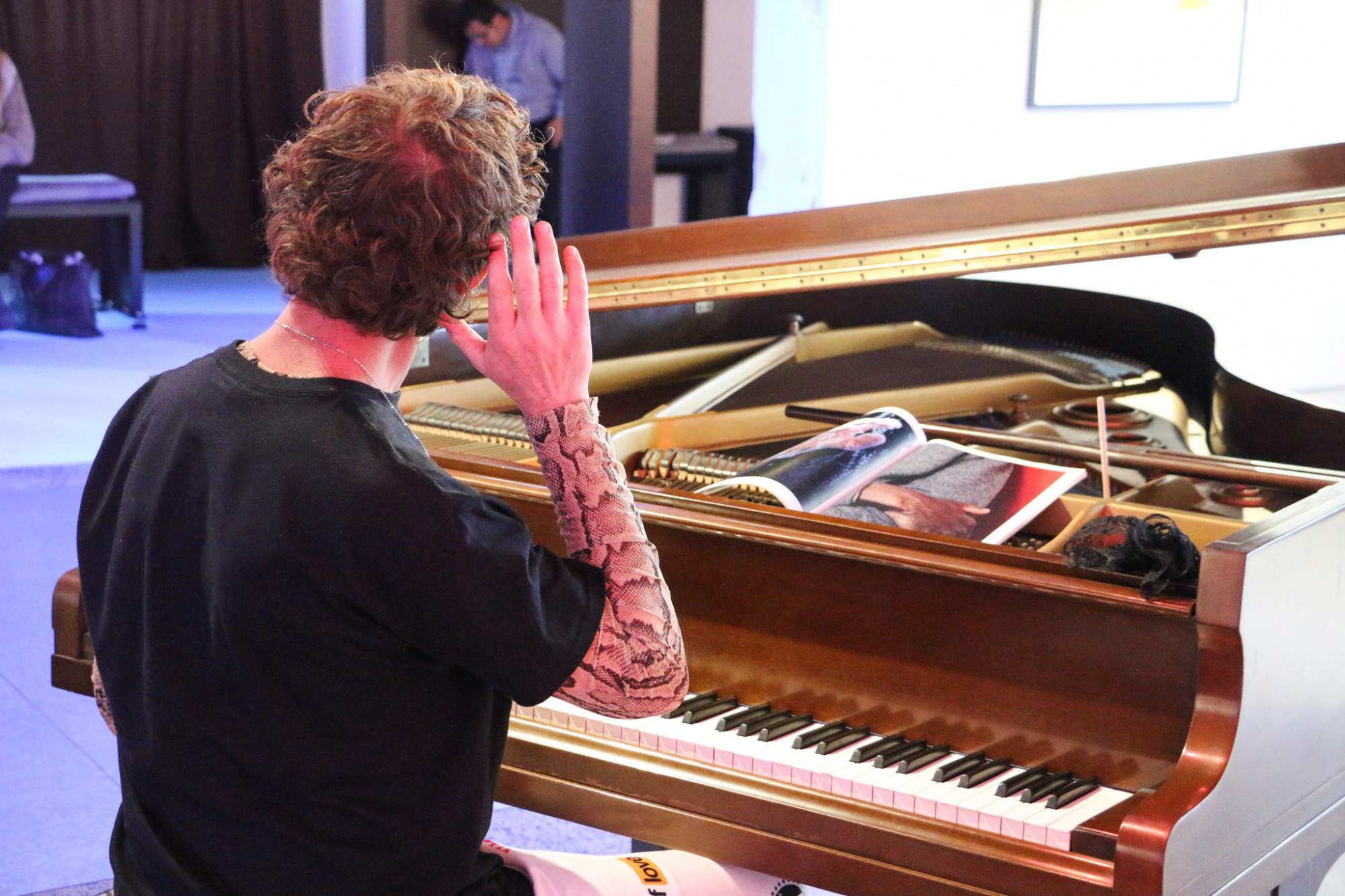 A person is sat at the piano holding their hand open to their ear, a booklet of hand images is on the piano.