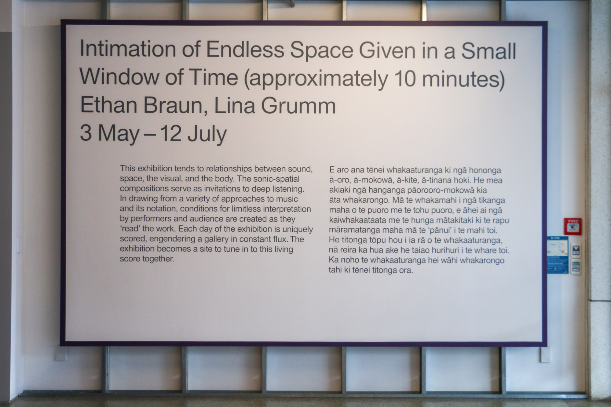 Image of exhibition wall text on a large board with a grey text and purple border hung on the gallery wall.