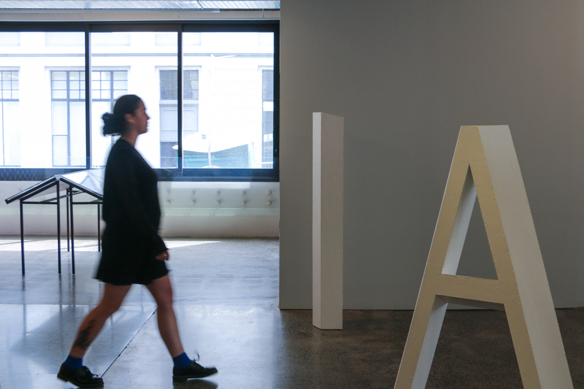 A person is walking through the gallery, between the brown vitrines and through the large sculptural letters.