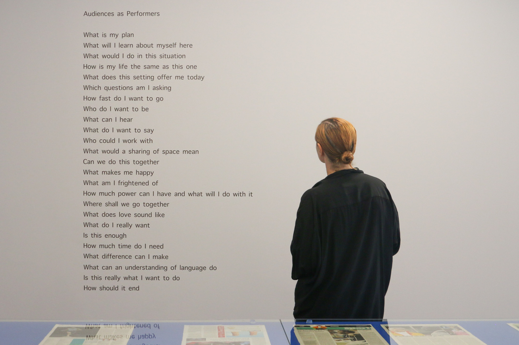 A person looks at a poem written with brown vinyl text on a grey wall.