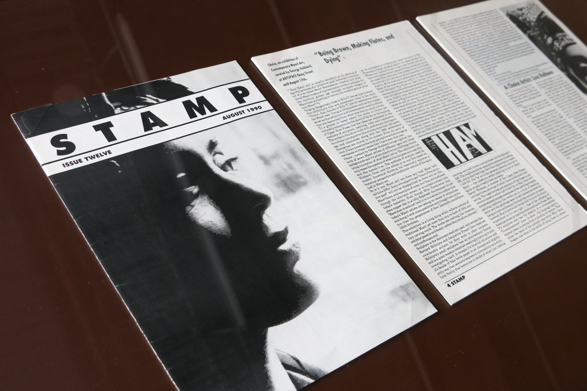 Close up of a vitrine, painted brown with glass on top of a magazine article with some black and white images.