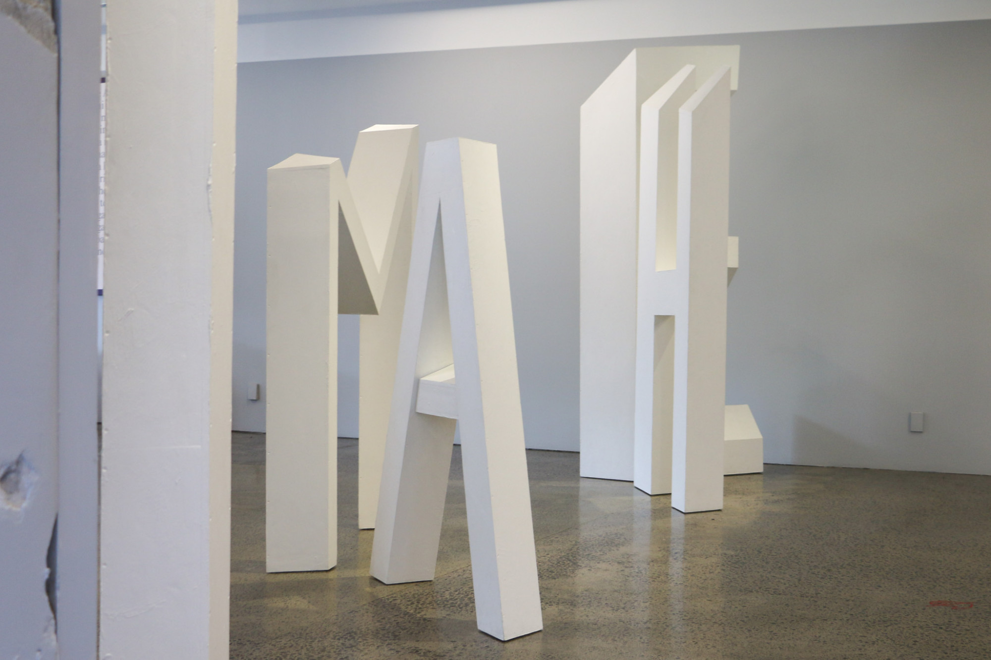 A side angle of a large white sculpture made out of letters, at this angle you can read slightly out of order they say 'I AM HE'