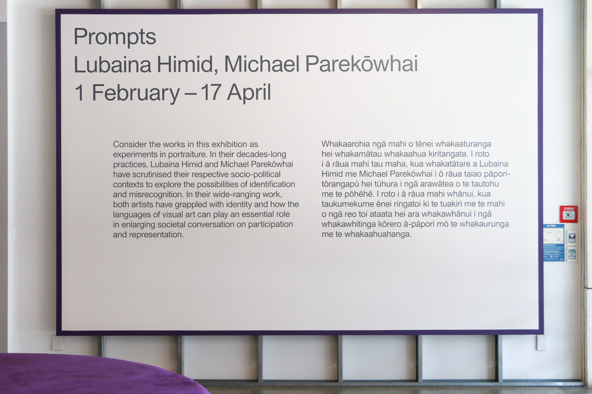 Image of exhibition wall text on a large board with a grey text and purple border hung on the gallery wall.