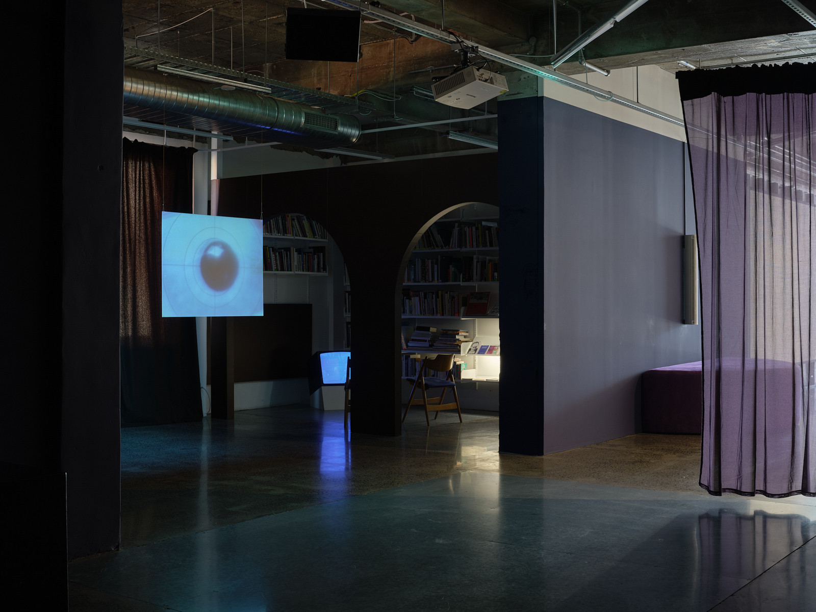 A hanging screen is in the background with a sheer curtain to the right, another room can be seen in the background.