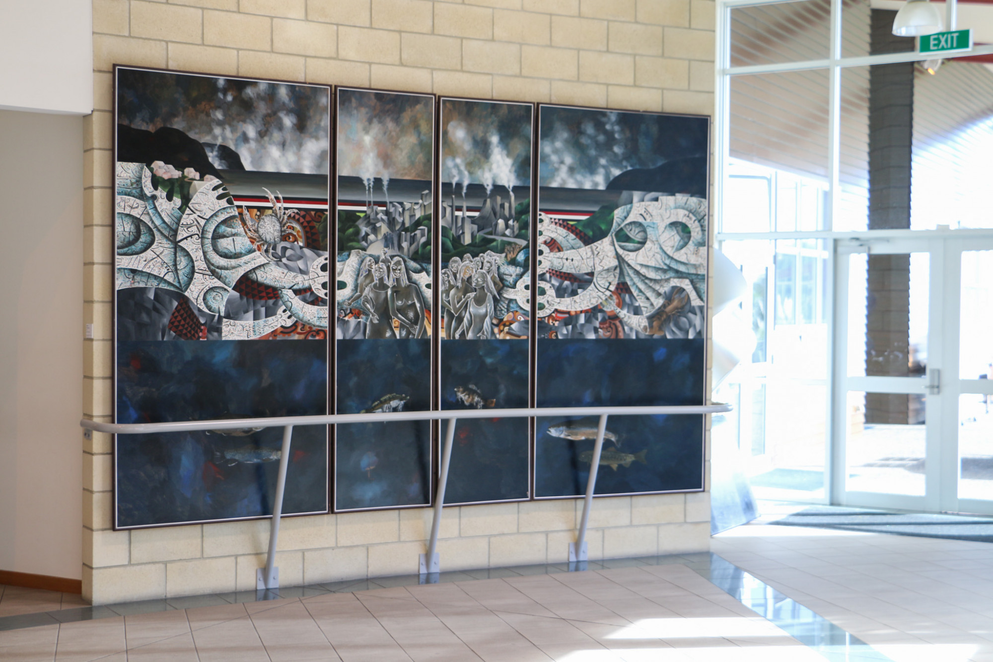 A large painting which depicts a landscape with abstract figures covers a wall in a buildings foyer.
