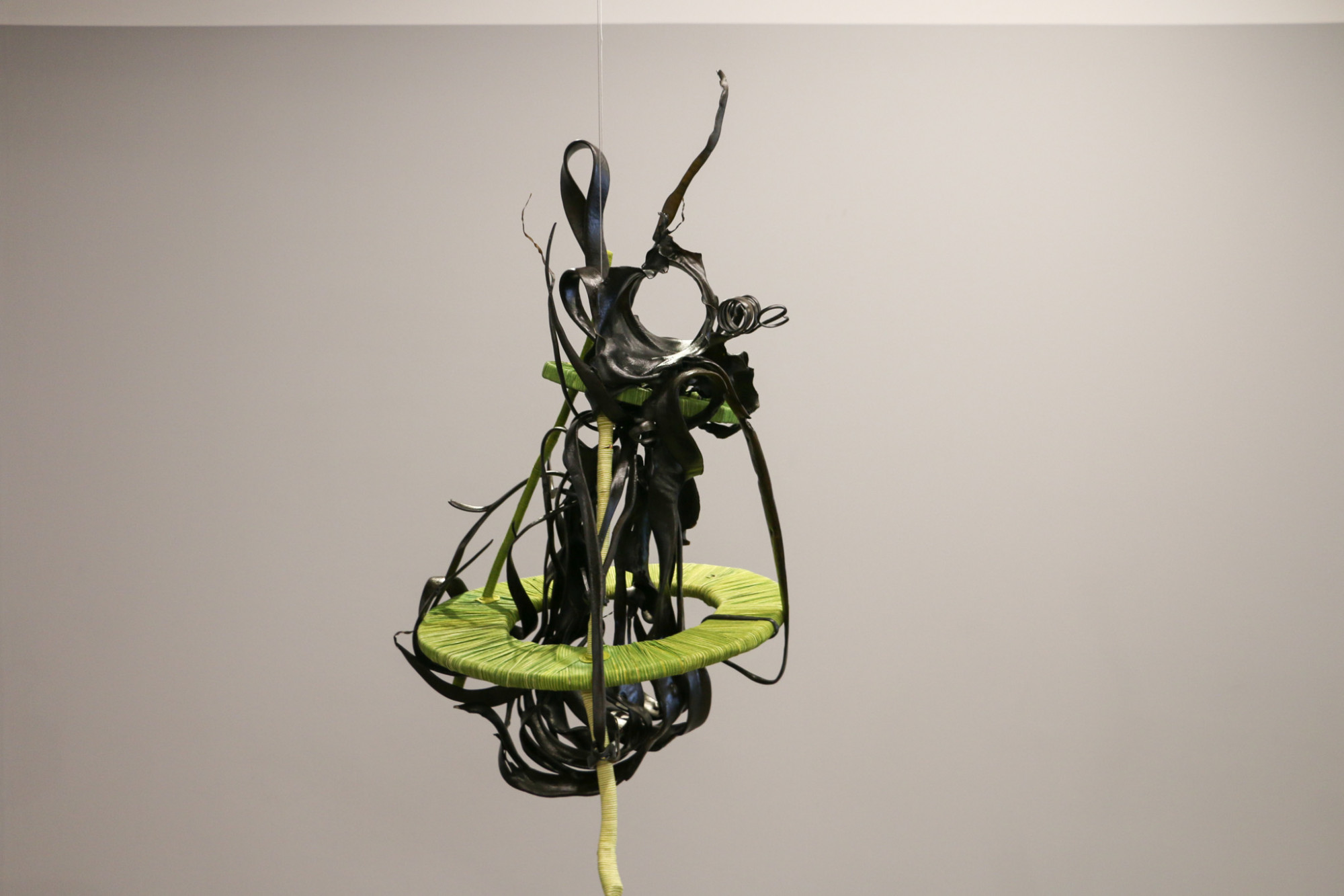 A sculpture is suspended from the ceiling, it is made of  seaweed and driftwood coated in coloured cord.