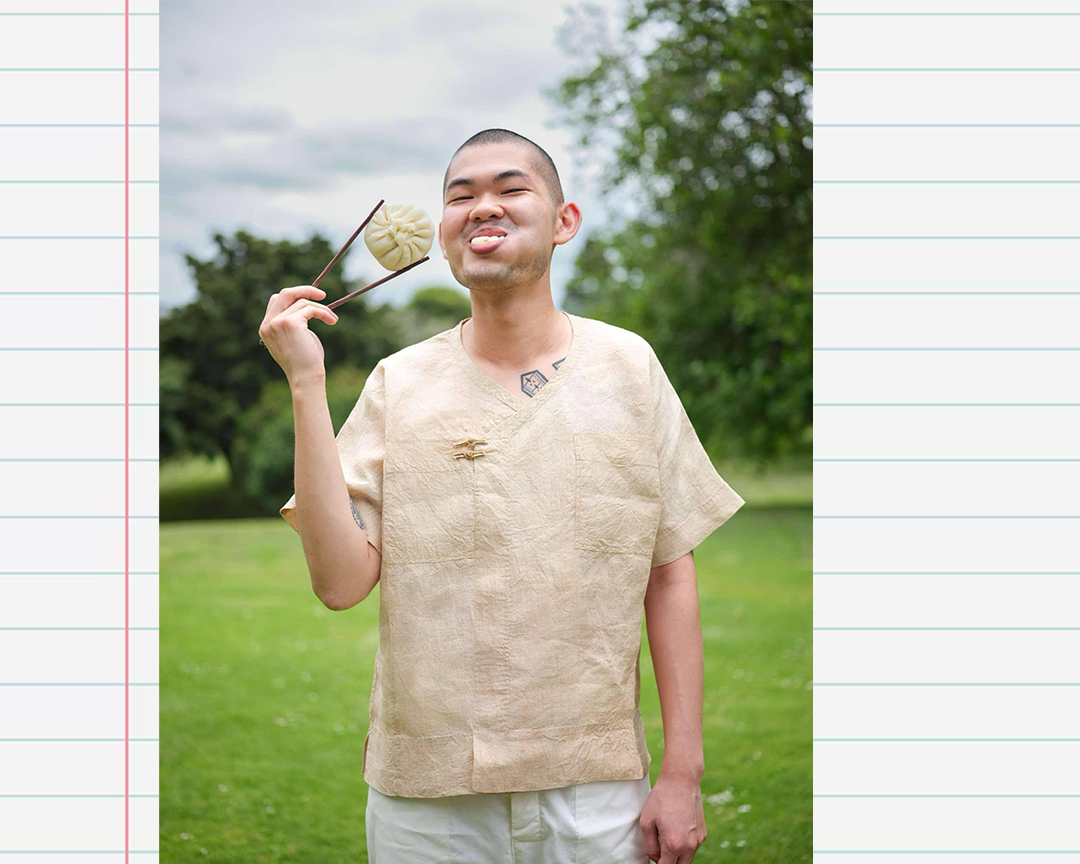 A headshot of Sam Low eating a bao bun on an exercise book paper background