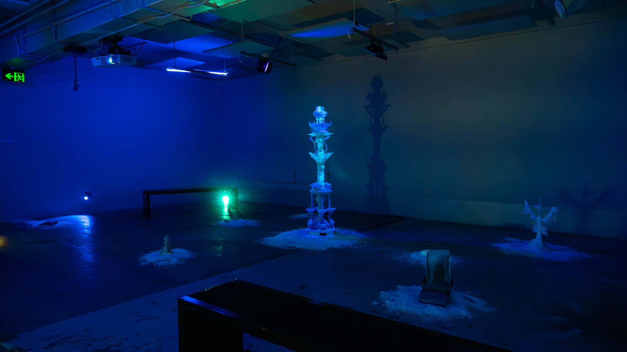 An illuminated sculpture is at the centre of a dark space, with small sculptures on the ground and black metal benches in the corner of the space