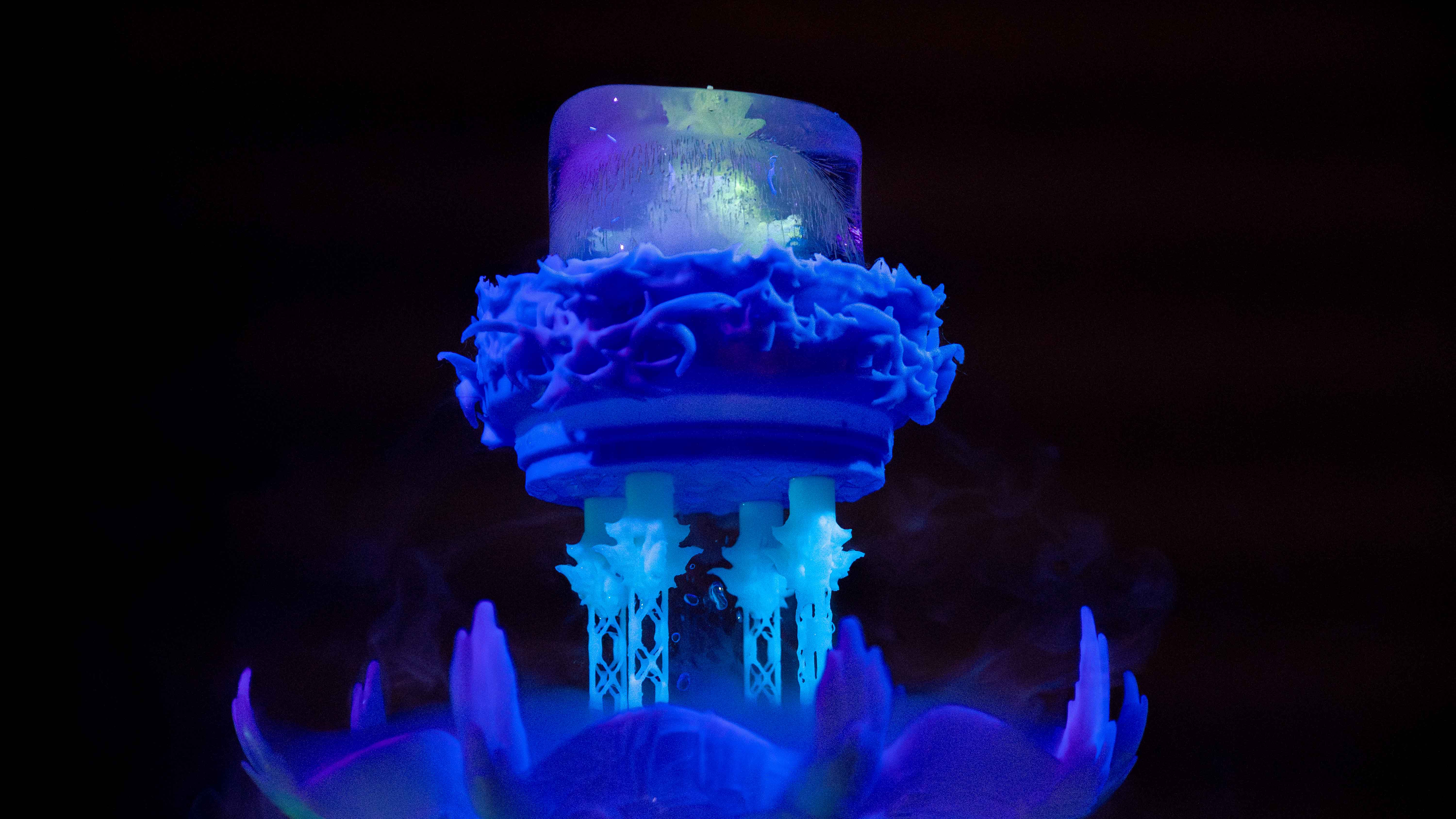 A glow in dark yellow sculpture frozen in a small tube of ice, which sits on top of a blue and green sculpture thawing into water and mist