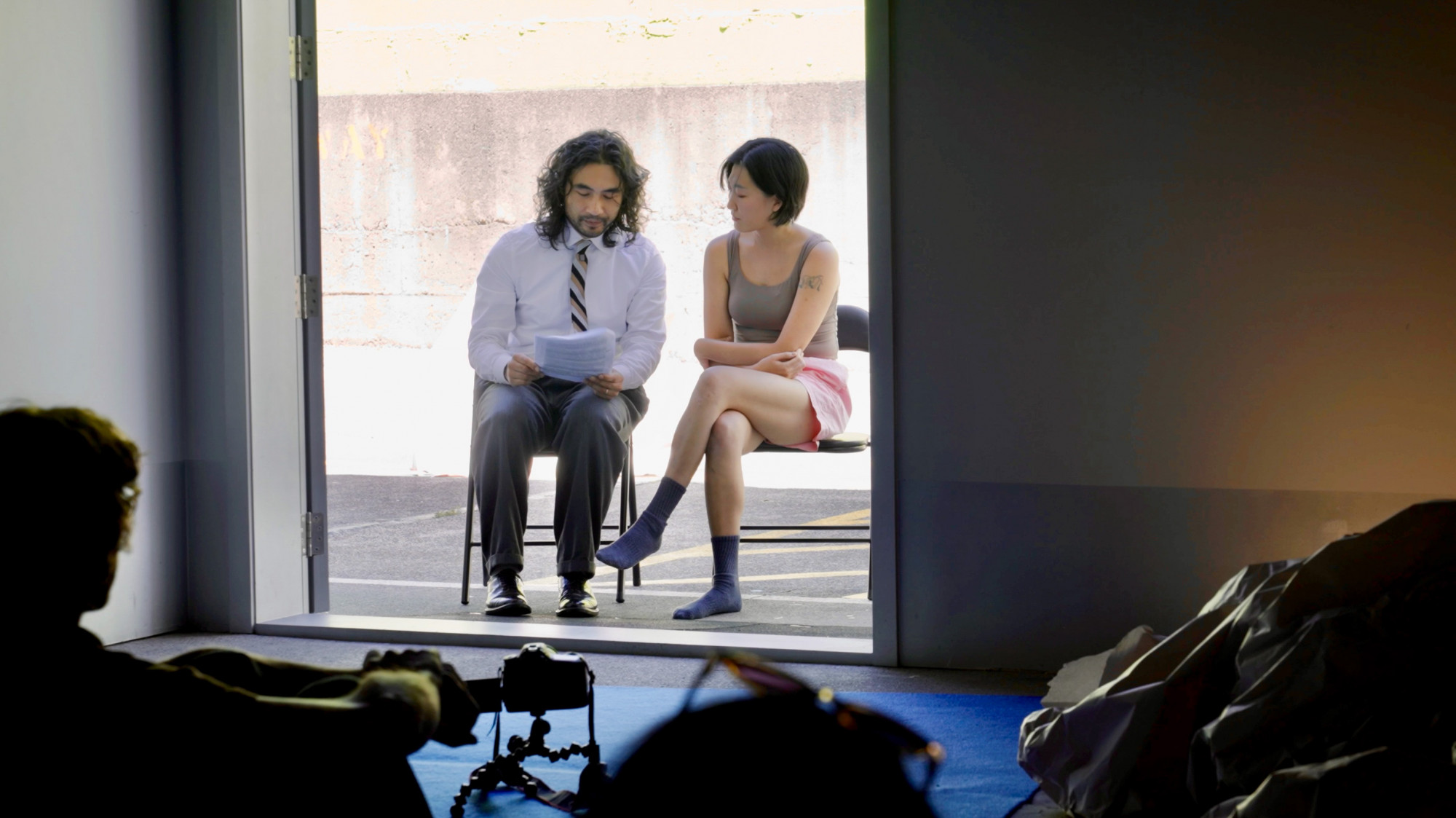 One man in shirt and one woman in singlet and pink shorts sitting next to each other at the entrance of a space