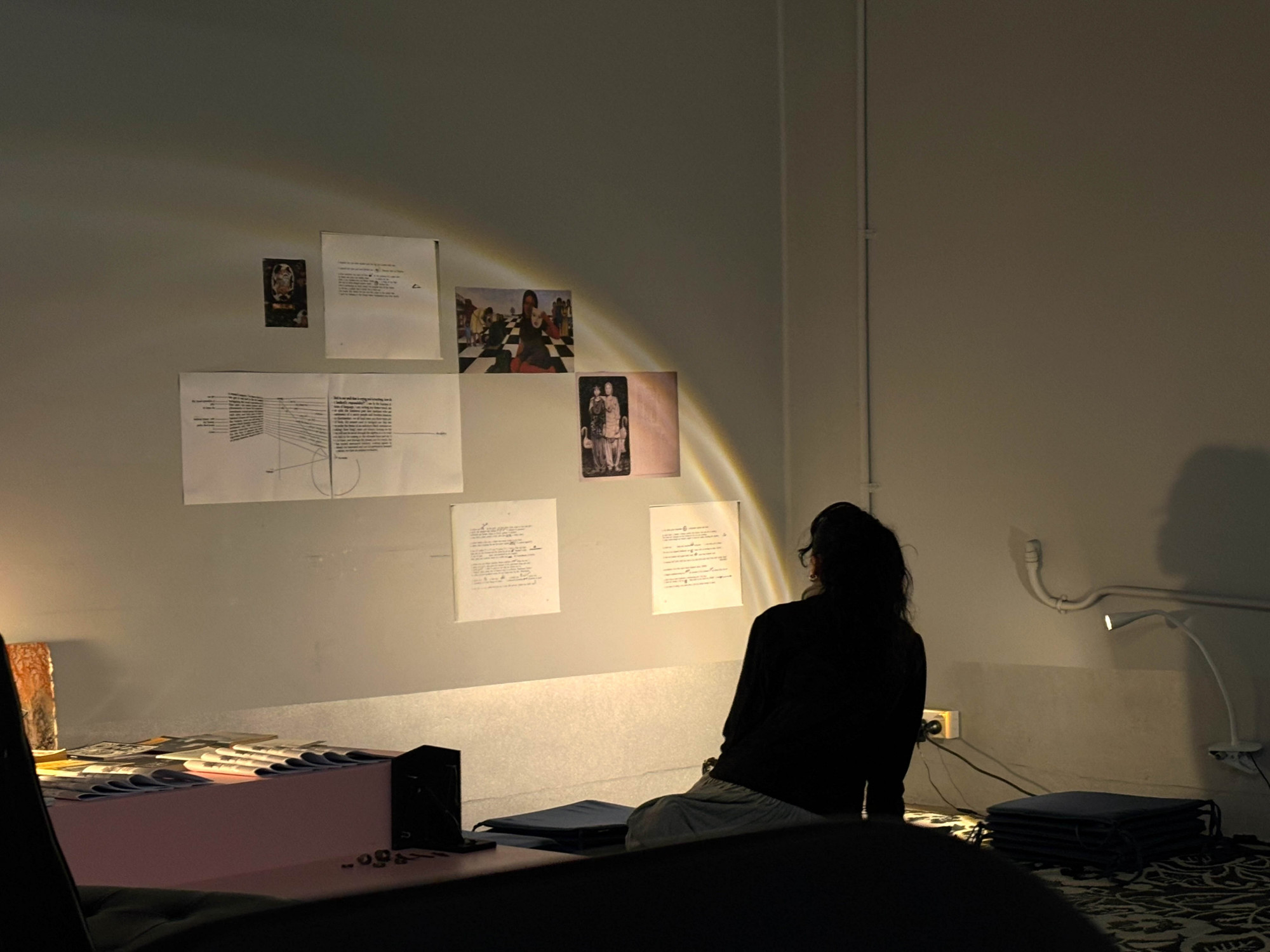 The back of a person sitting on the ground while looking up at the wall with many printed texts