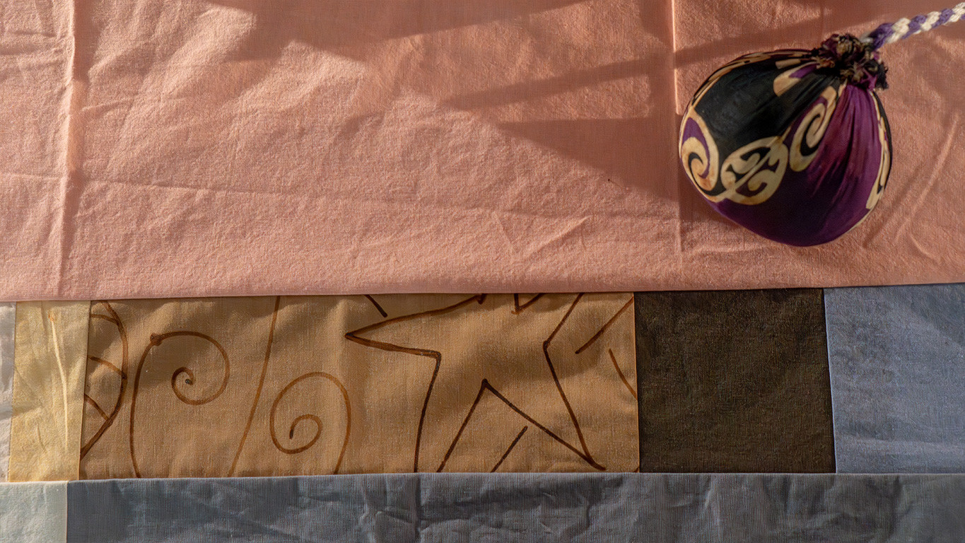 A purple and black poi placed on a pink quilt with hand drawn patterns