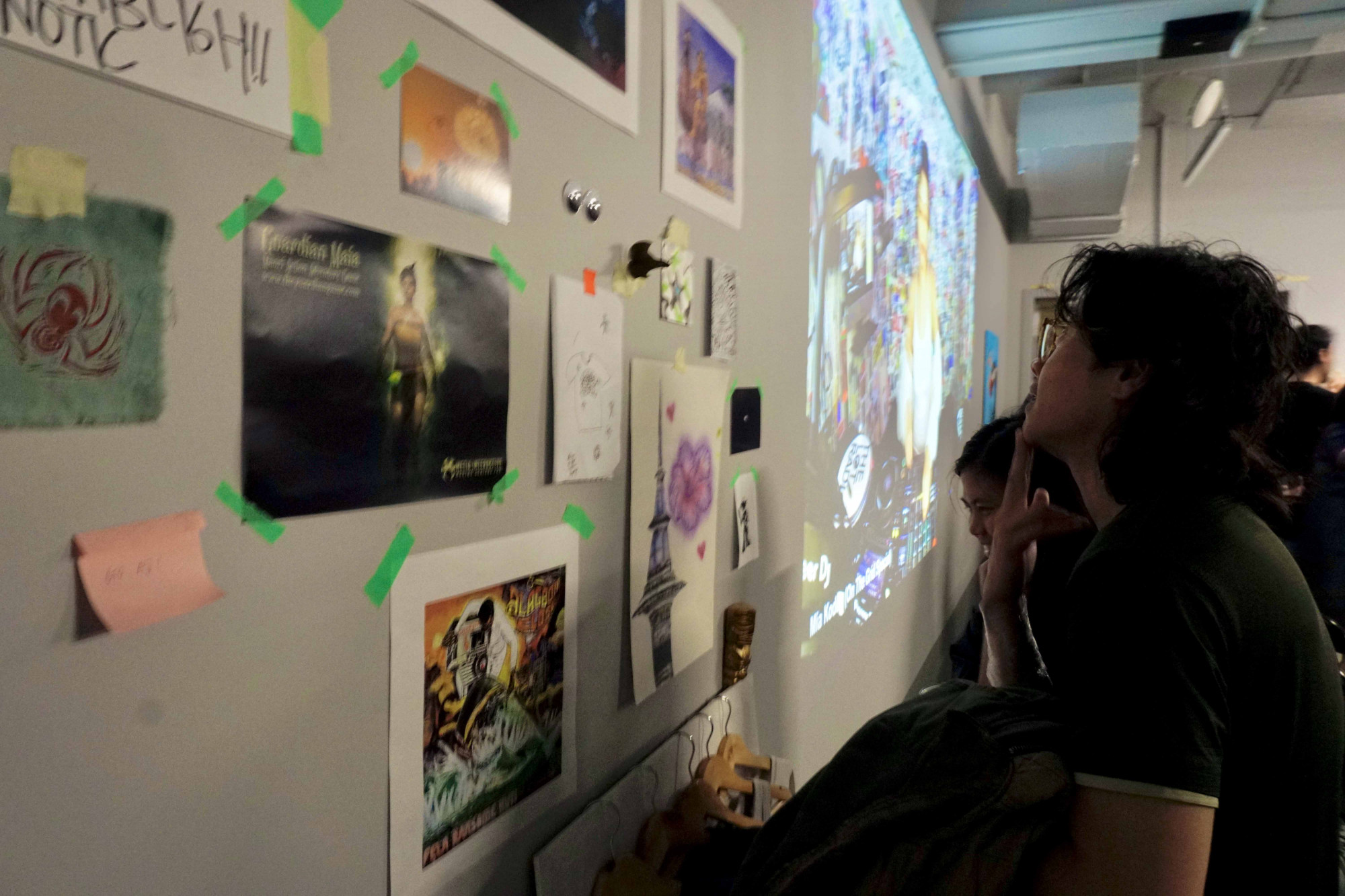 Two people looking at a wall of posters and illustrations.